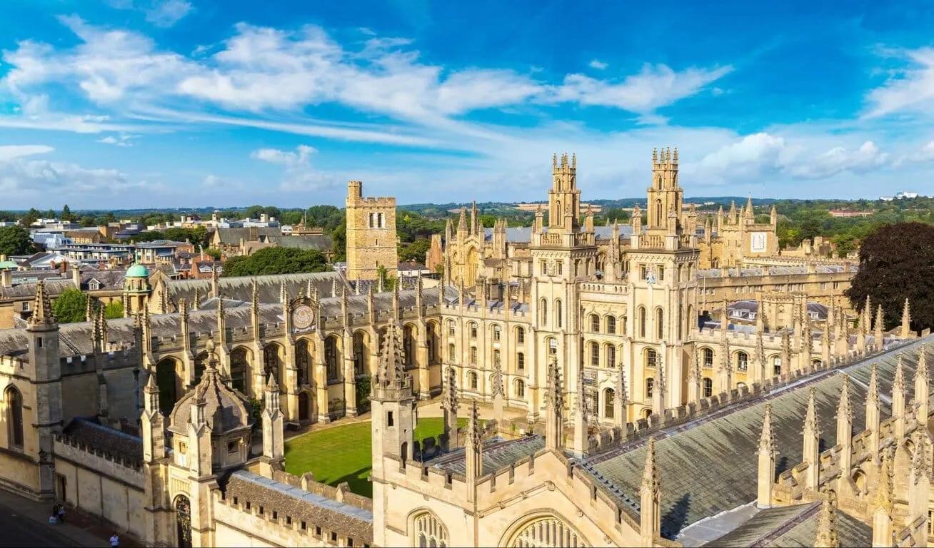 Aerial view of a historic university building with tall spires and intricate architecture, surrounded by a town and lush greenery.
