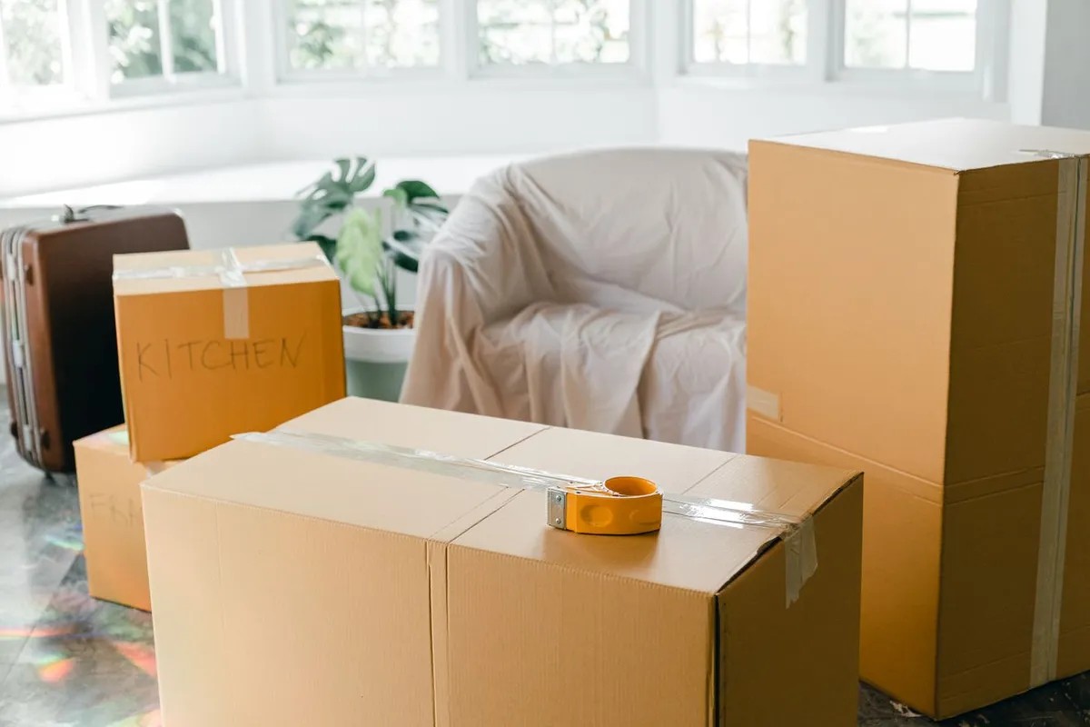 An armchair covered with a white sheet next to stacked cardboard boxes in a bright room