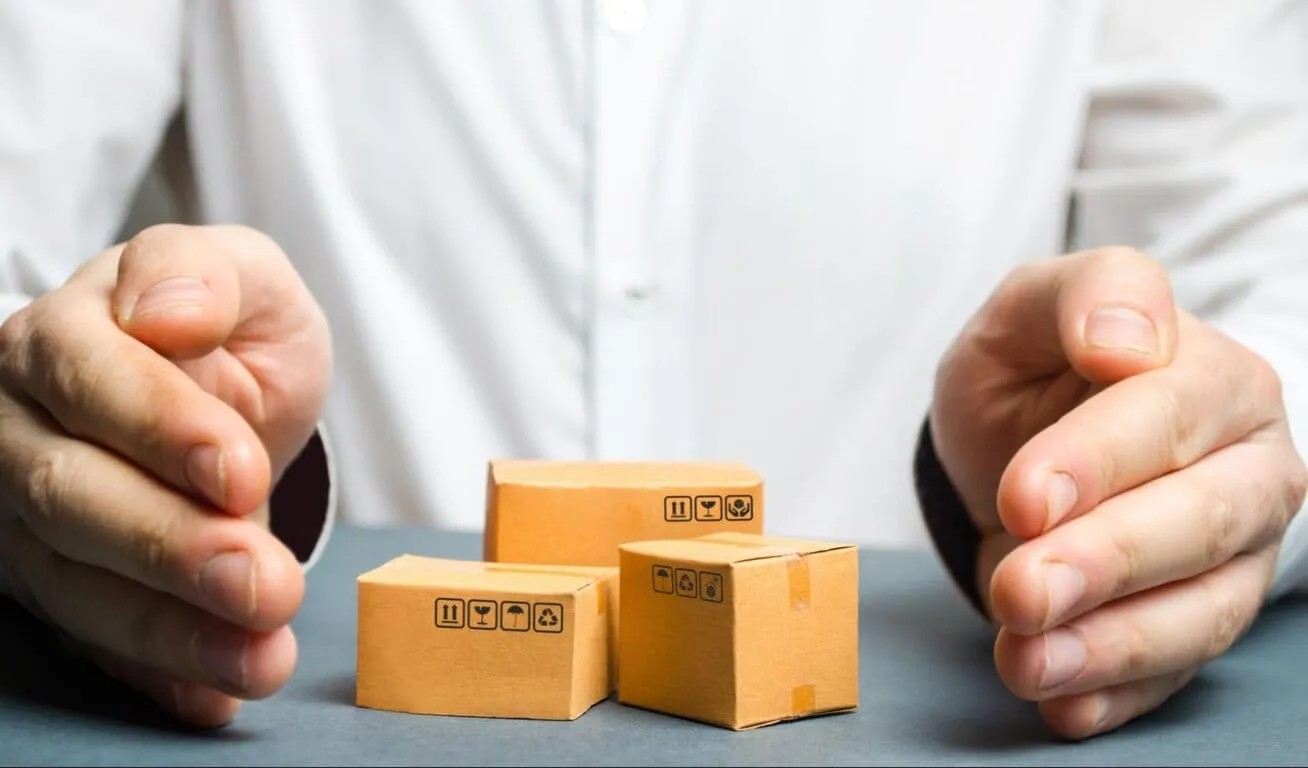 Protective Hands Over Miniature Cardboard Boxes Close-up of a person’s hands protecting miniature cardboard boxes representing parcel protection or insurance concept.