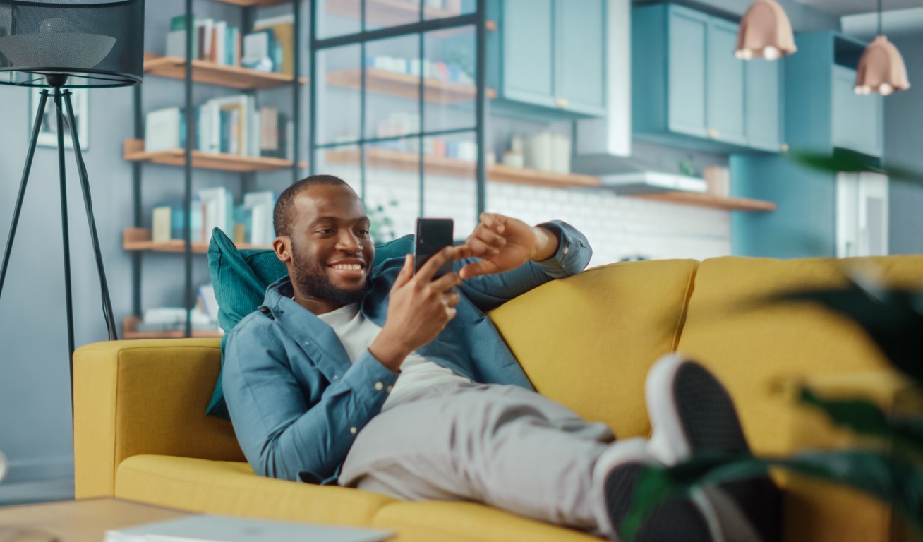 Man smiling while using a smartphone on a yellow couch